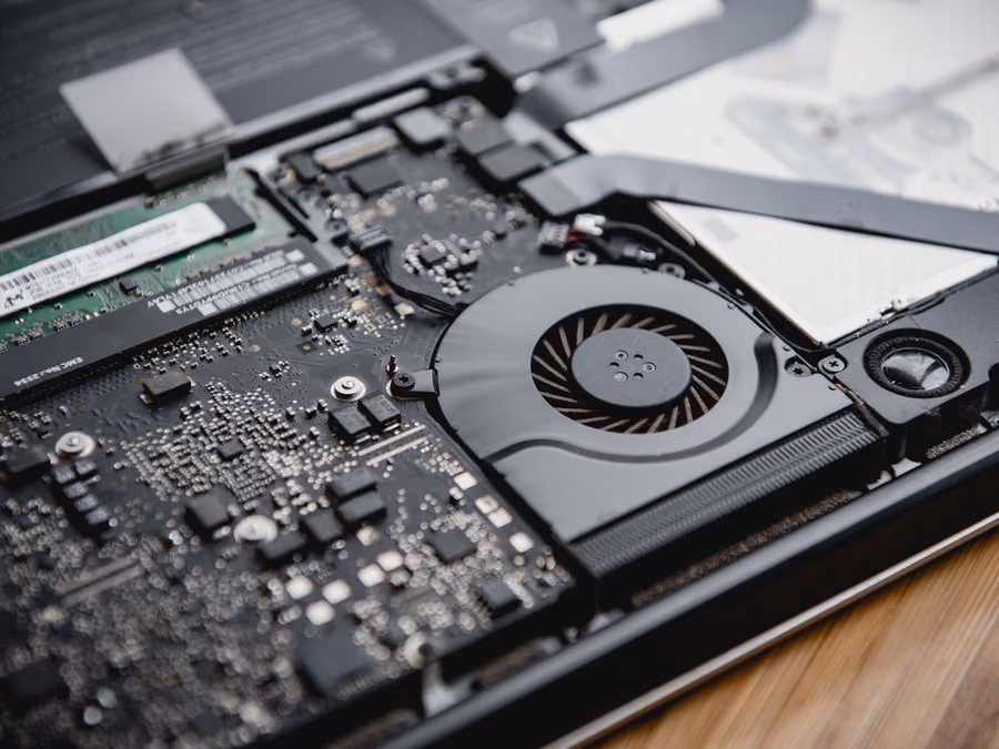 An opened laptop on a bench with its logic board and cooling visible
